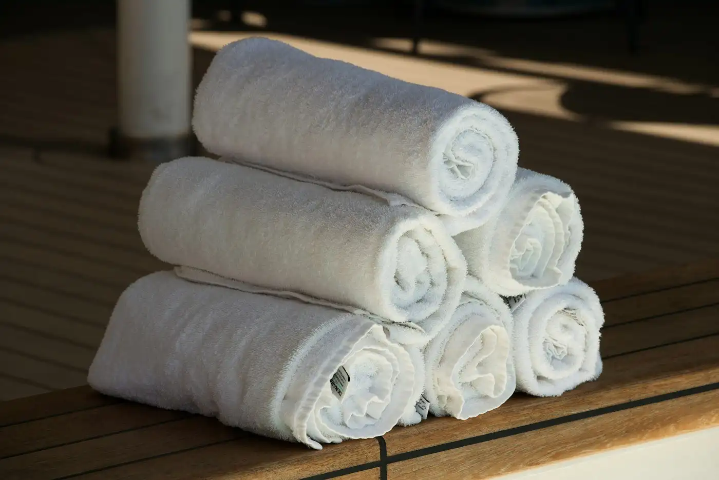 Six rolled white towels stacked on a wooden bench
