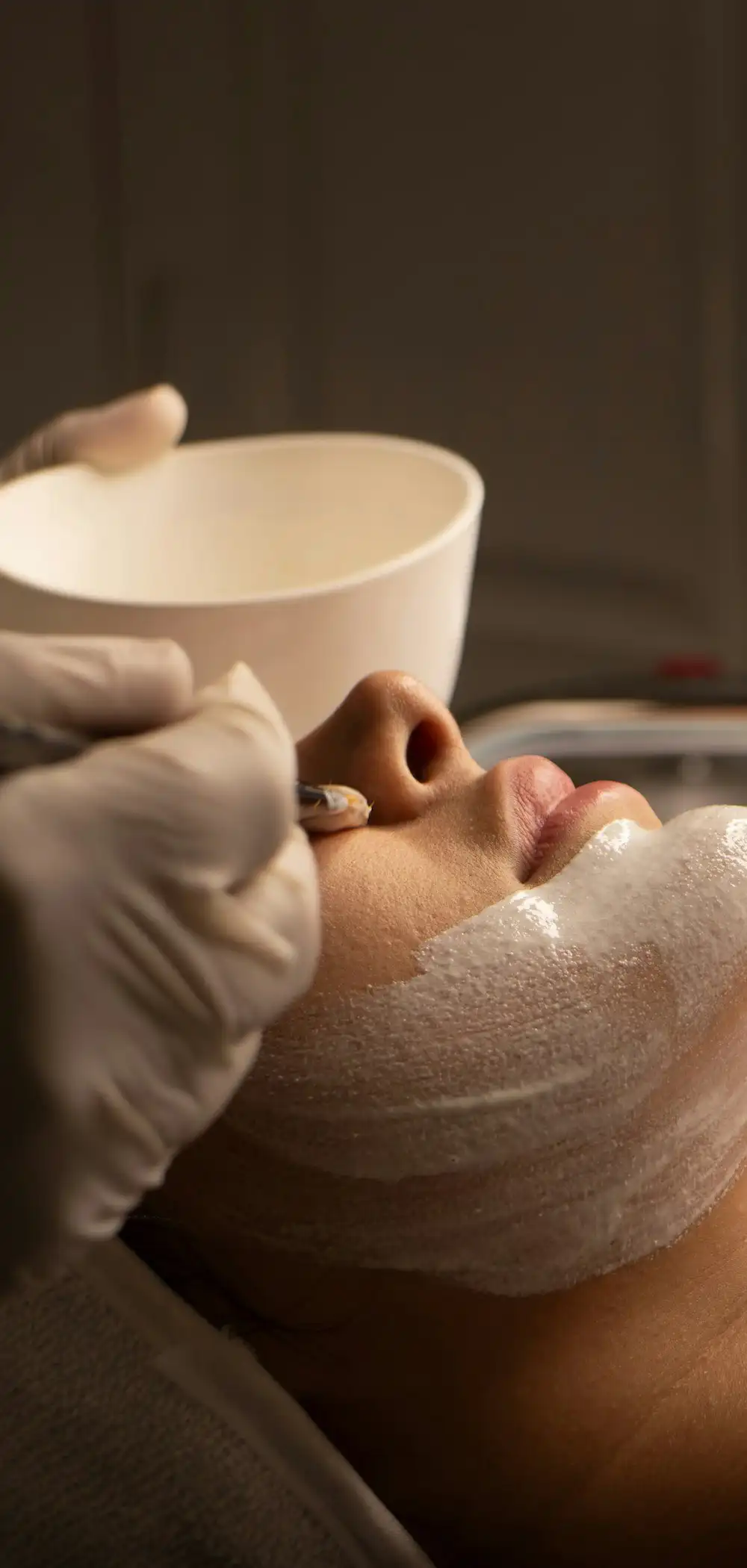 An aesthetician's gloved hands applying a cream mask during a facial
