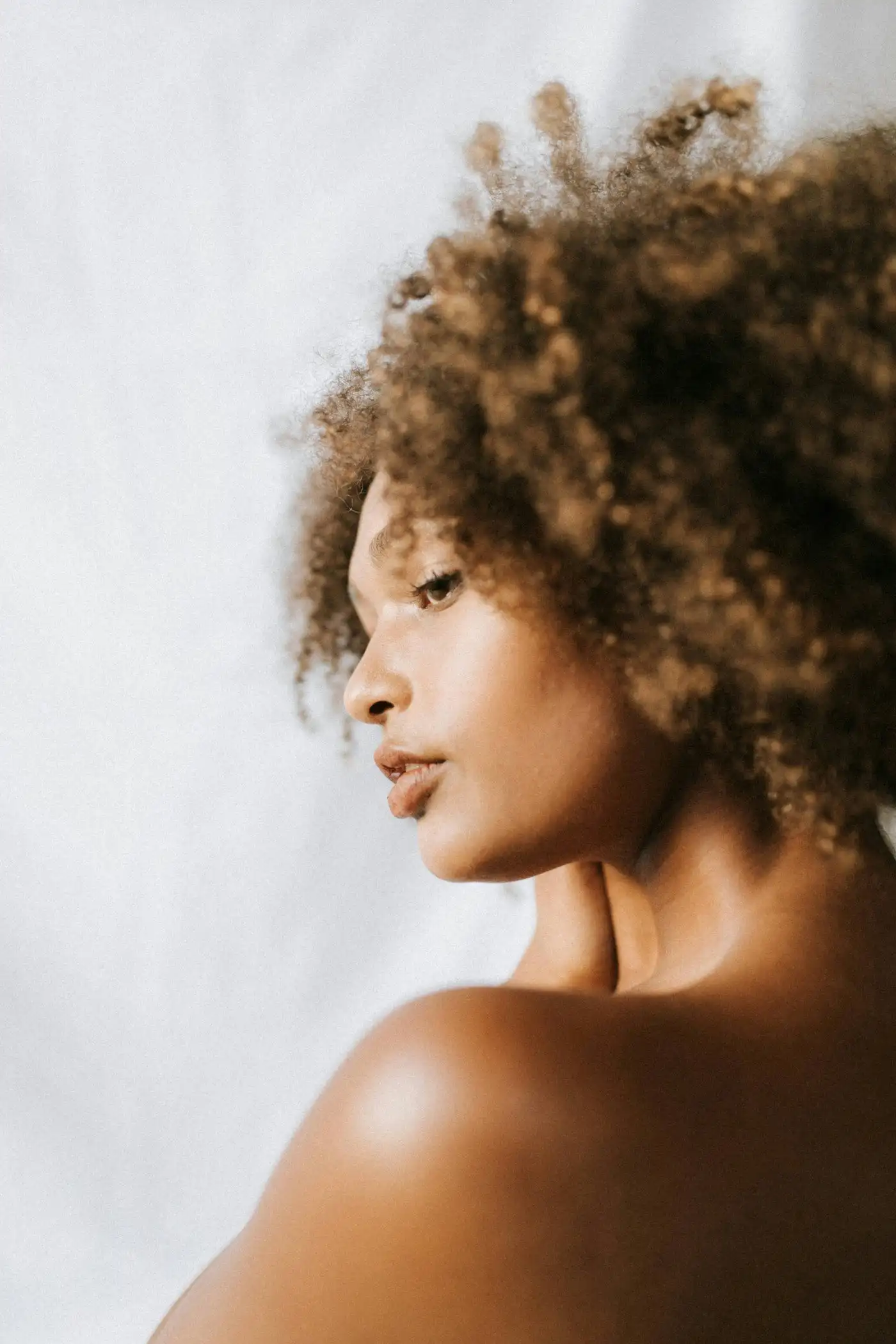 A woman with natural curly hair looking to the side in soft daylight