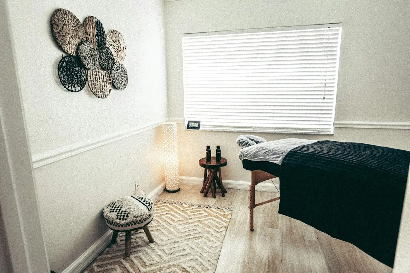 A calm treatment room with a padded table, a small stool and window blinds