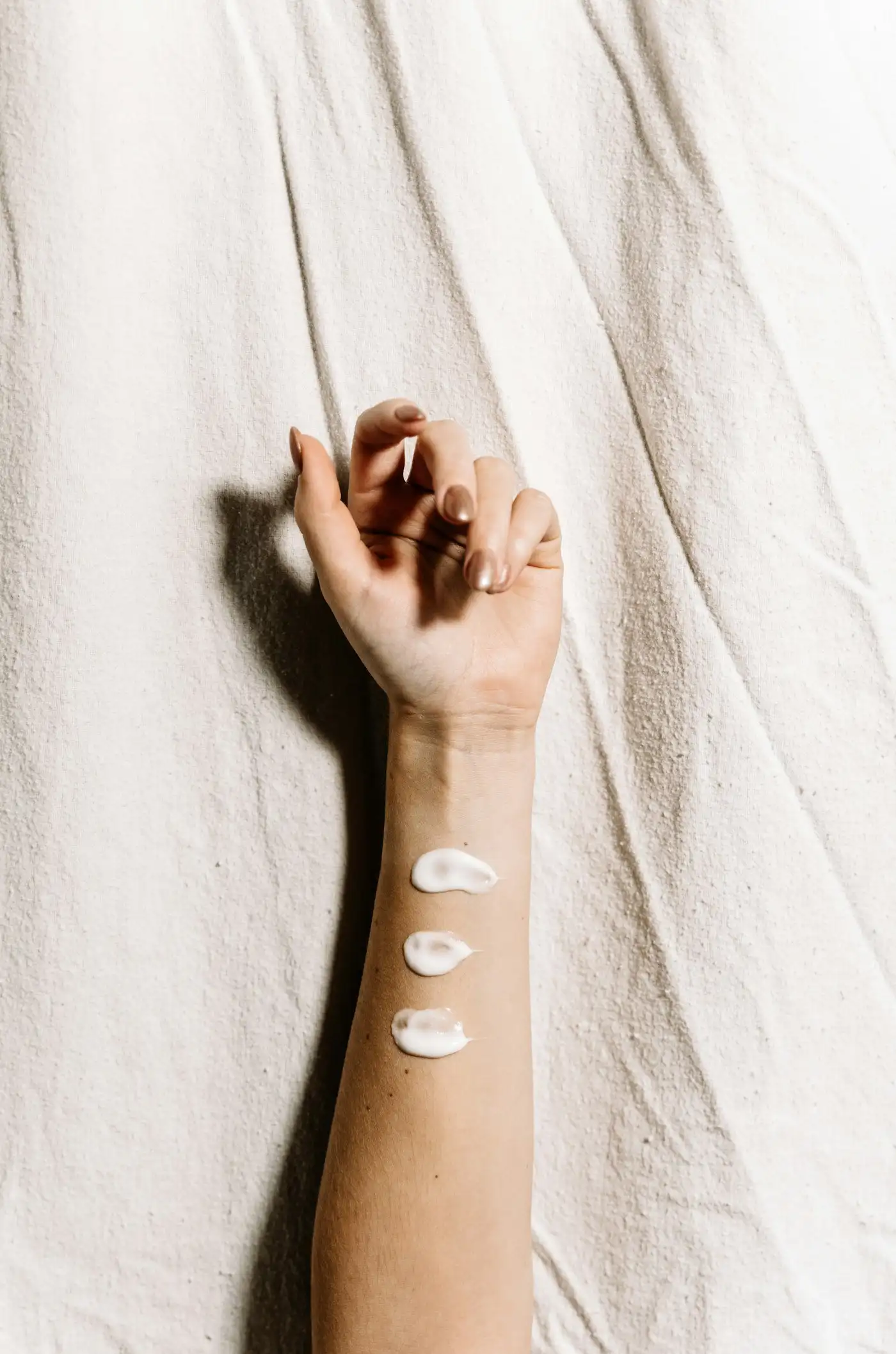 Three dabs of white cream on the inside of a forearm, resting on a linen sheet